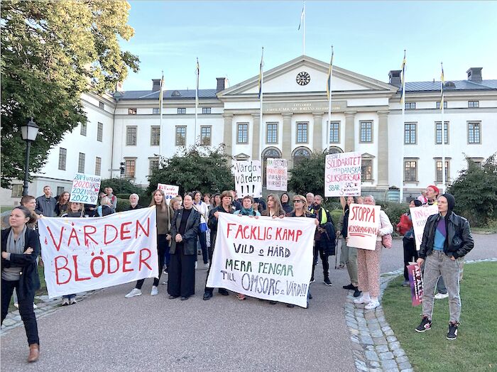 En grupp arbetare har samlats för att protestera mot ohållbar vård och omsorg. De håller i skyltar med slagord.